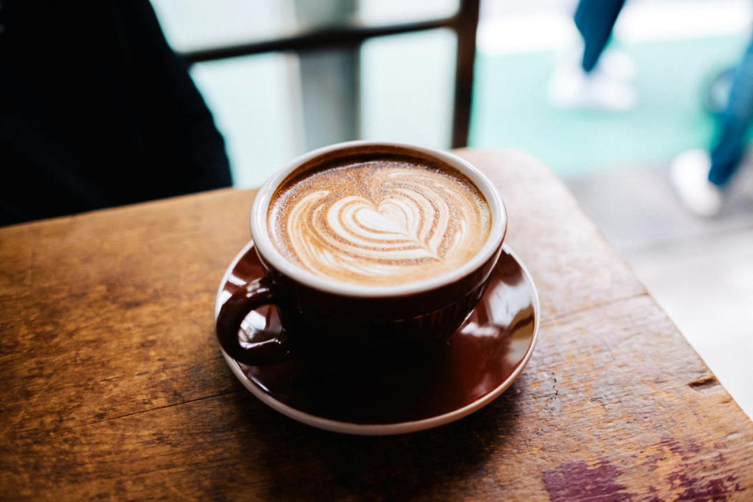 Šolja latte kafe sa srcem od mlečne pene na drvenom stolu